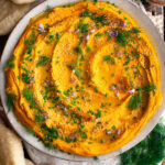 Paprika Roasted Carrot Hummus on a plate with herbs and sesame seeds on top