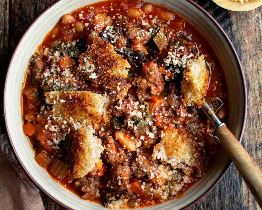 a bowl of ribollita soup with Italian sausage and toasted bread