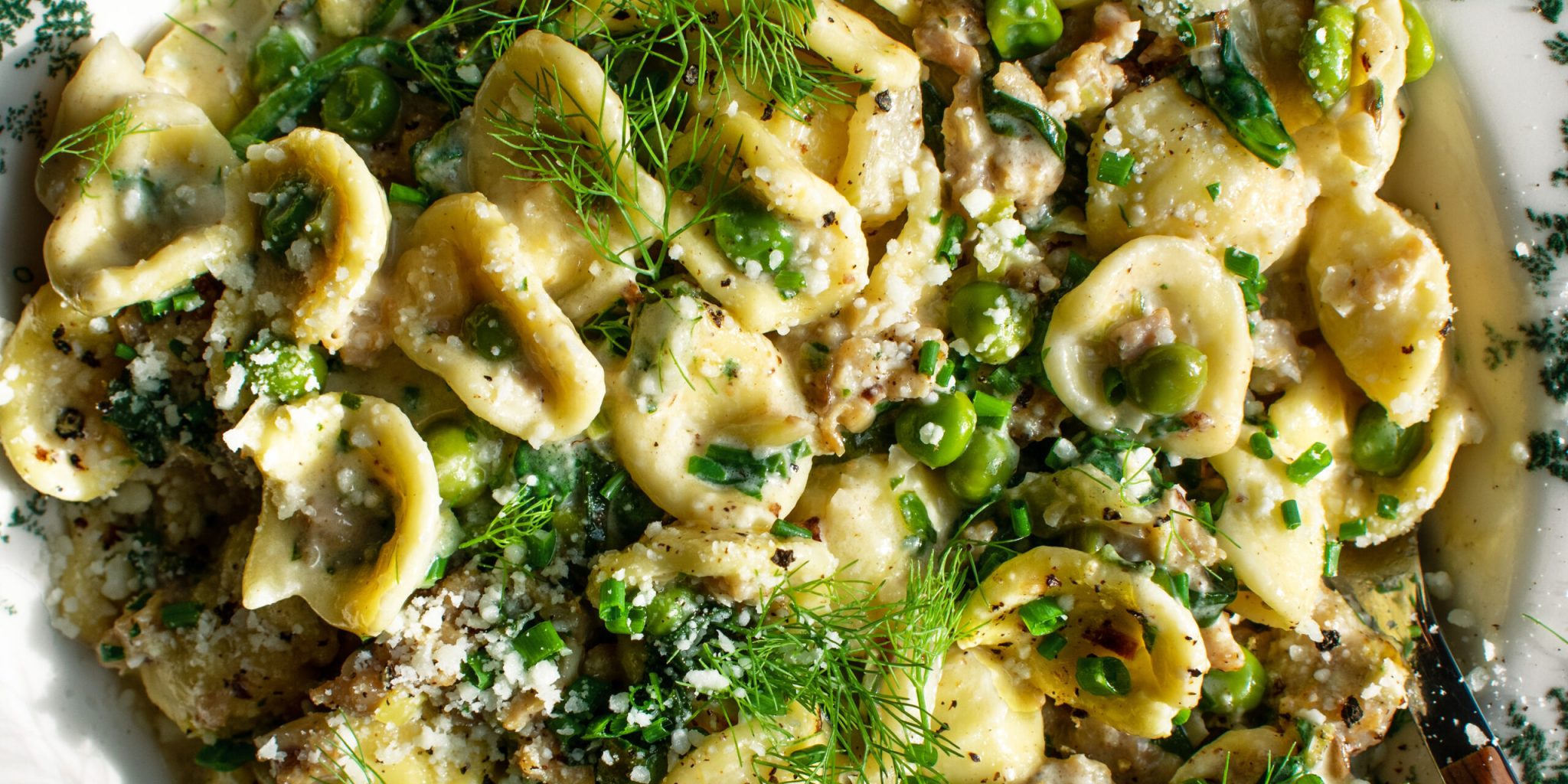 finished dish of Creamy Orecchiette with chicken sausage & spring vegetables in a bowl with herbs and cheese on top