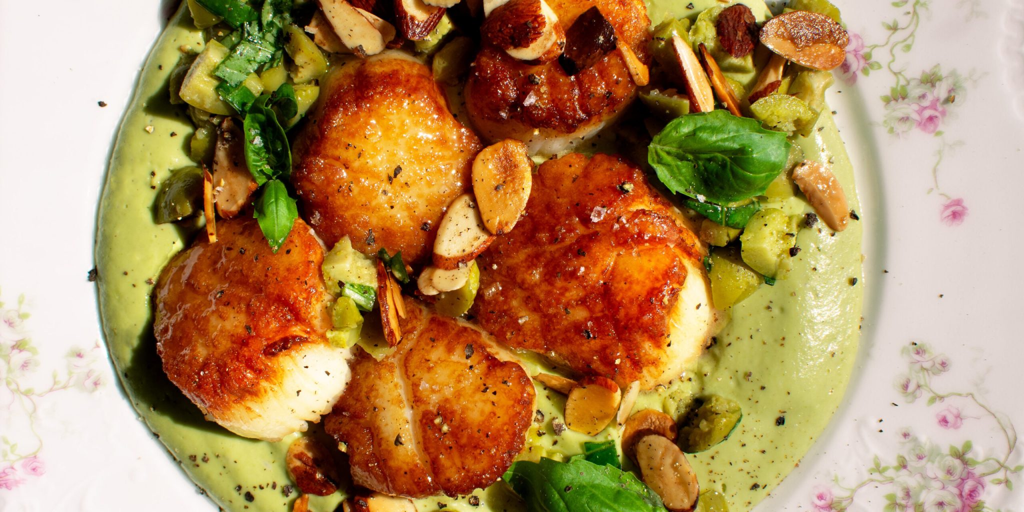 a plate of seared scallops over whipped cauliflower with olives and toasted almonds